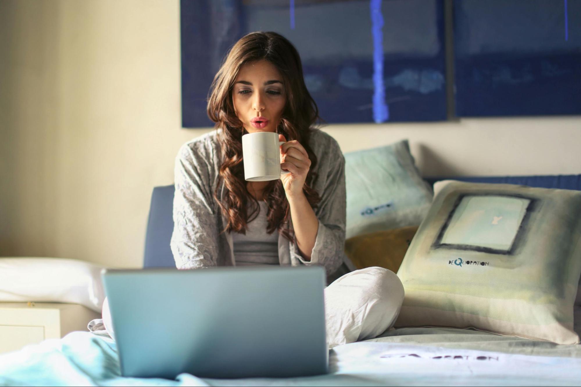 A woman holding a mug and using a laptop.