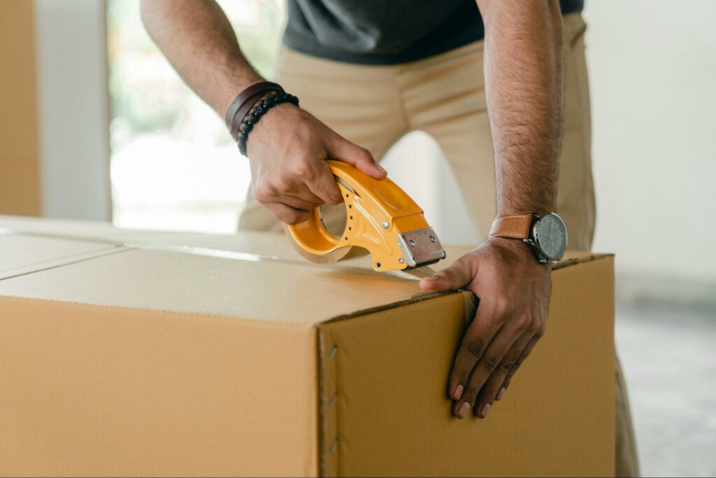 A man sealing a cardboard box with tape.