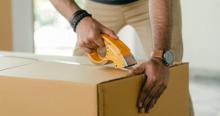 A man sealing a cardboard box with tape.