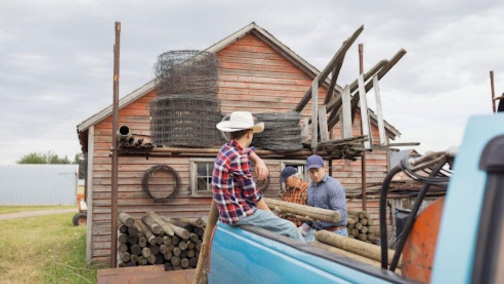 Homeowners and barn repair workers loading materials beside a wooden barn in New York, preparing for maintenance to protect stored belongings from damage.
